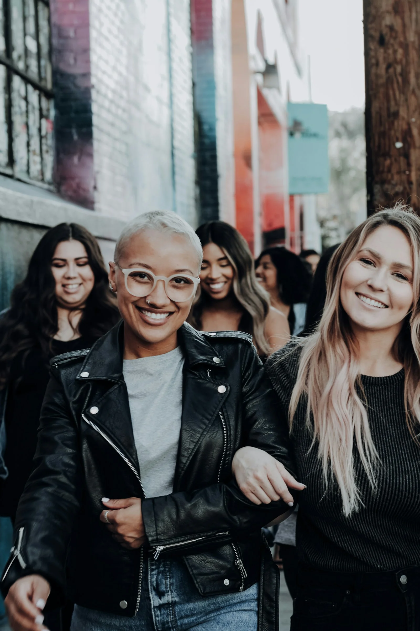 A group of women walking arm in arm down a colorful urban alleyway
