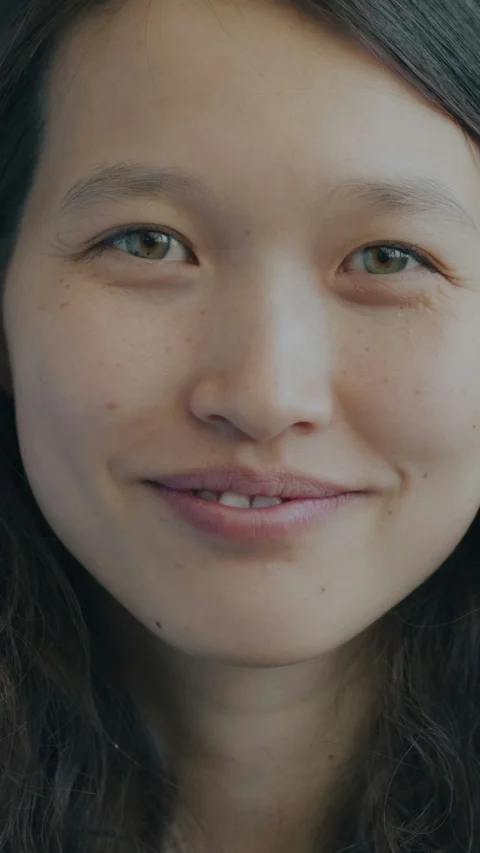 一位有雀斑與淡綠色眼睛的微笑女子特寫肖像