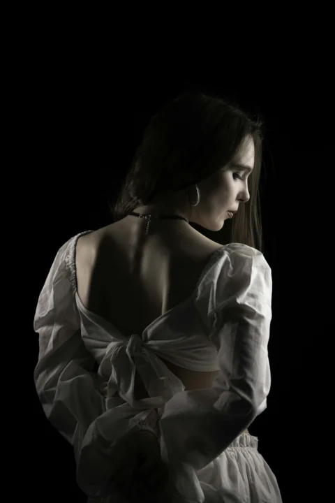 A woman in a white blouse with a tied back against a black background