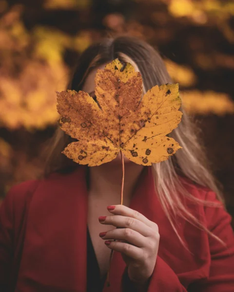 woman in red long sleeve shirt holding yellow maple leaf