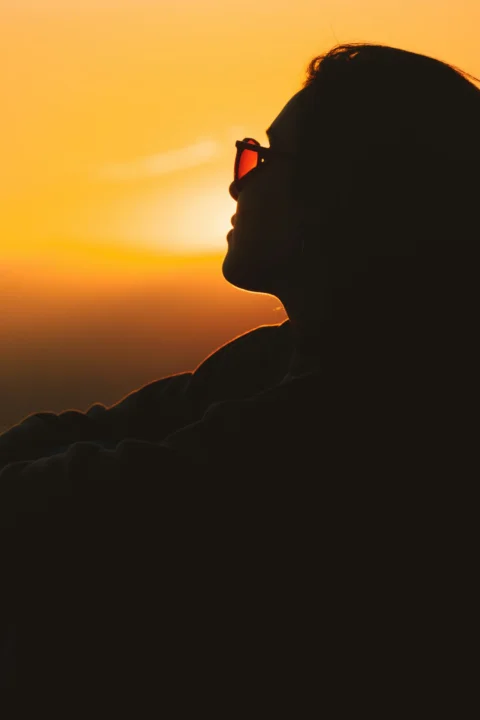 サングラスをかけて夕日を眺めている女性