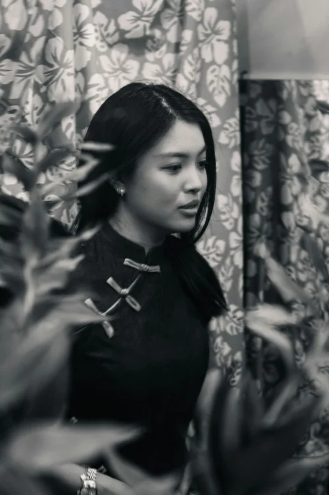 A young woman in a traditional dress stands by plants