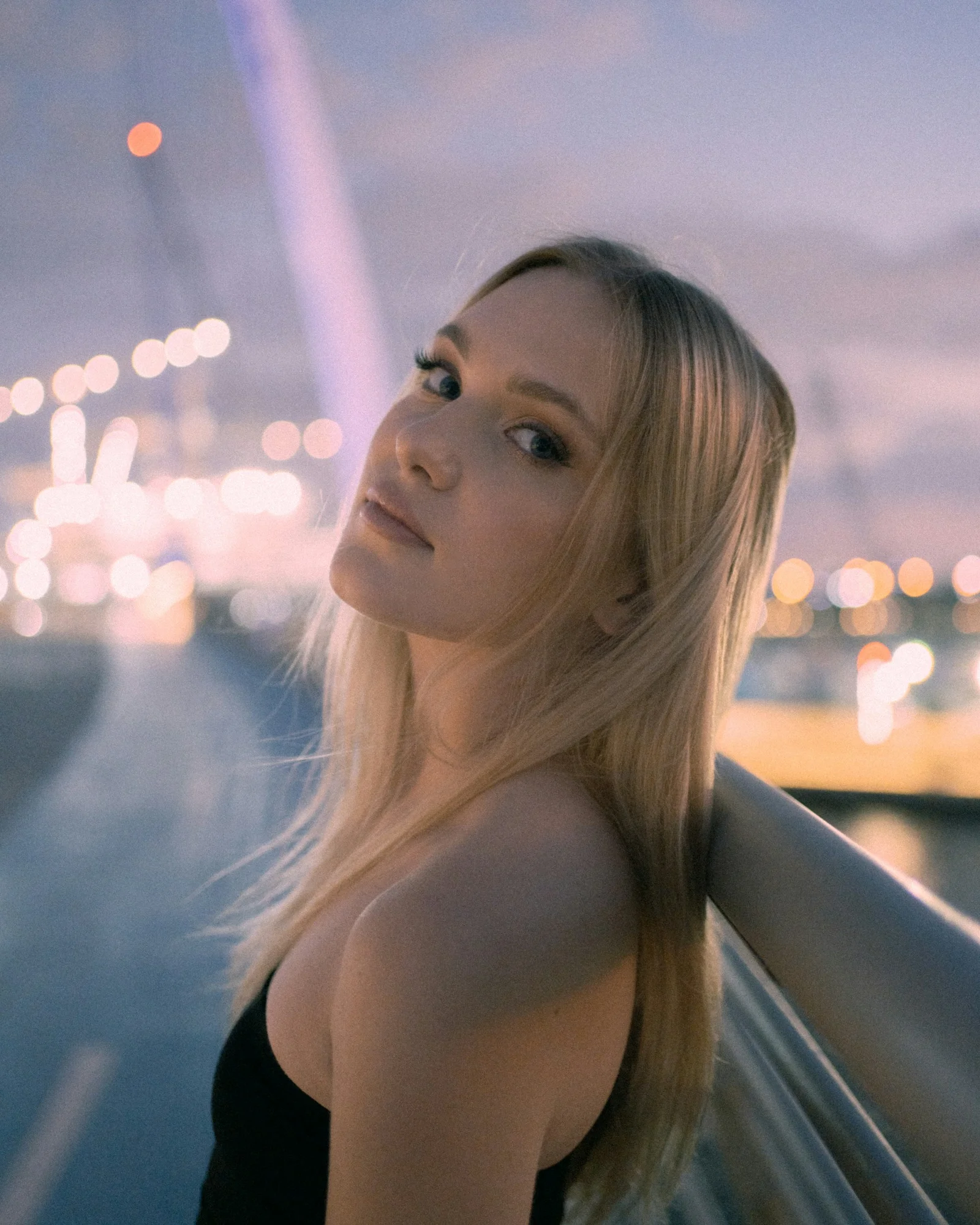 Blonde woman poses by a bridge at dusk