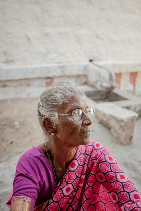 An old woman with glasses sitting on the ground