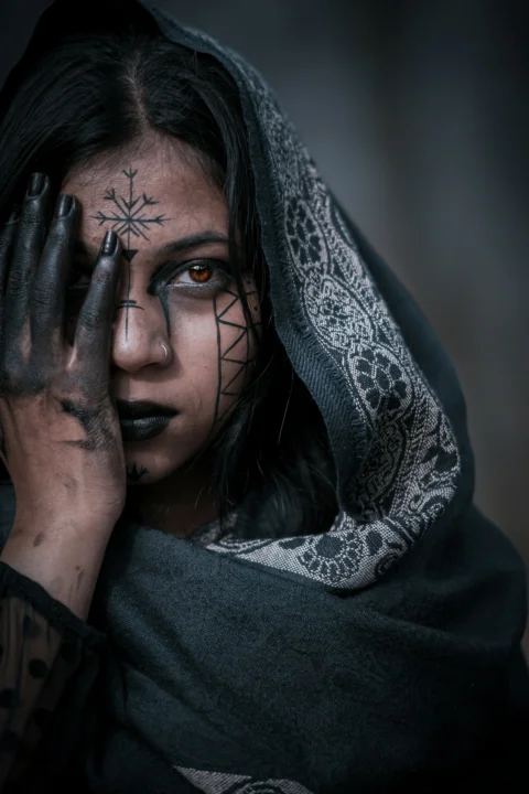 Woman with dark makeup and face paint covers eye