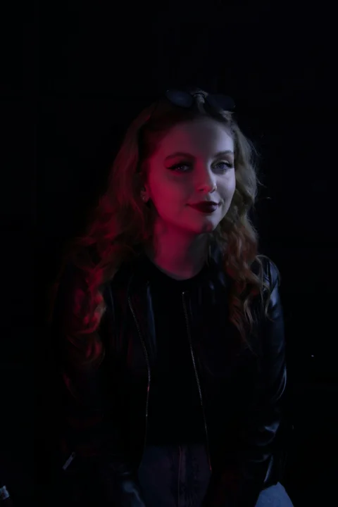 a woman in a black leather jacket sitting in a dark room