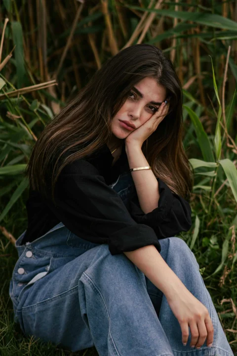 Young woman sitting in tall grass with hand on face