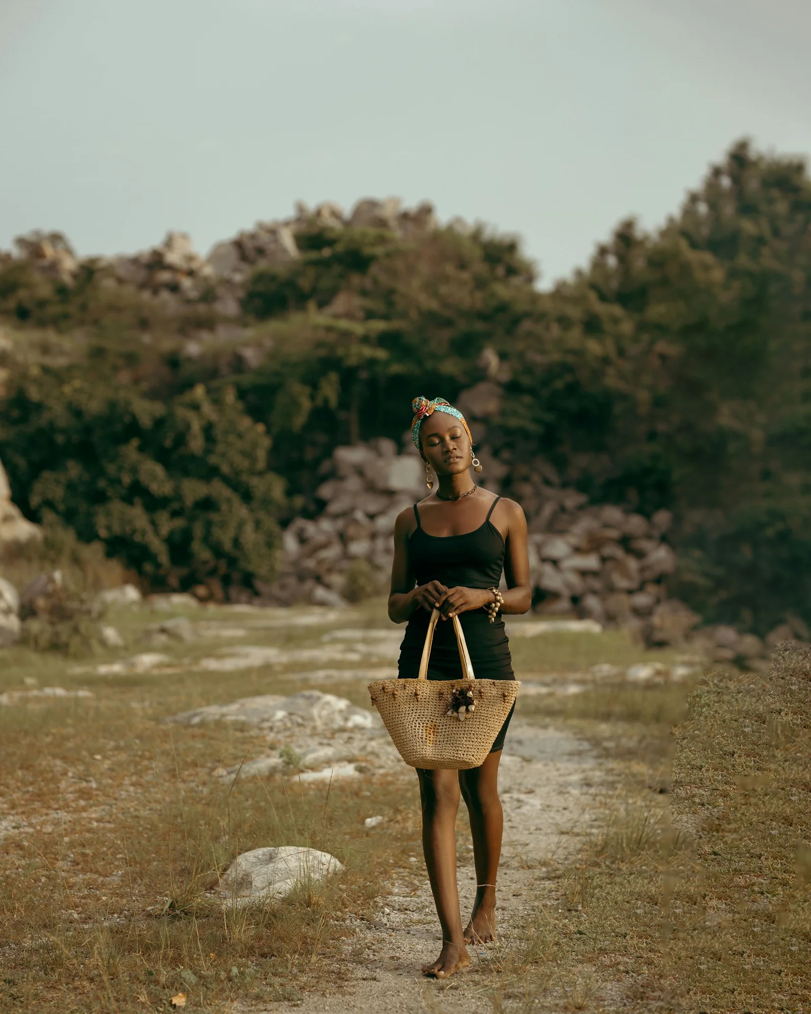 a woman walking down a dirt road carrying a bag