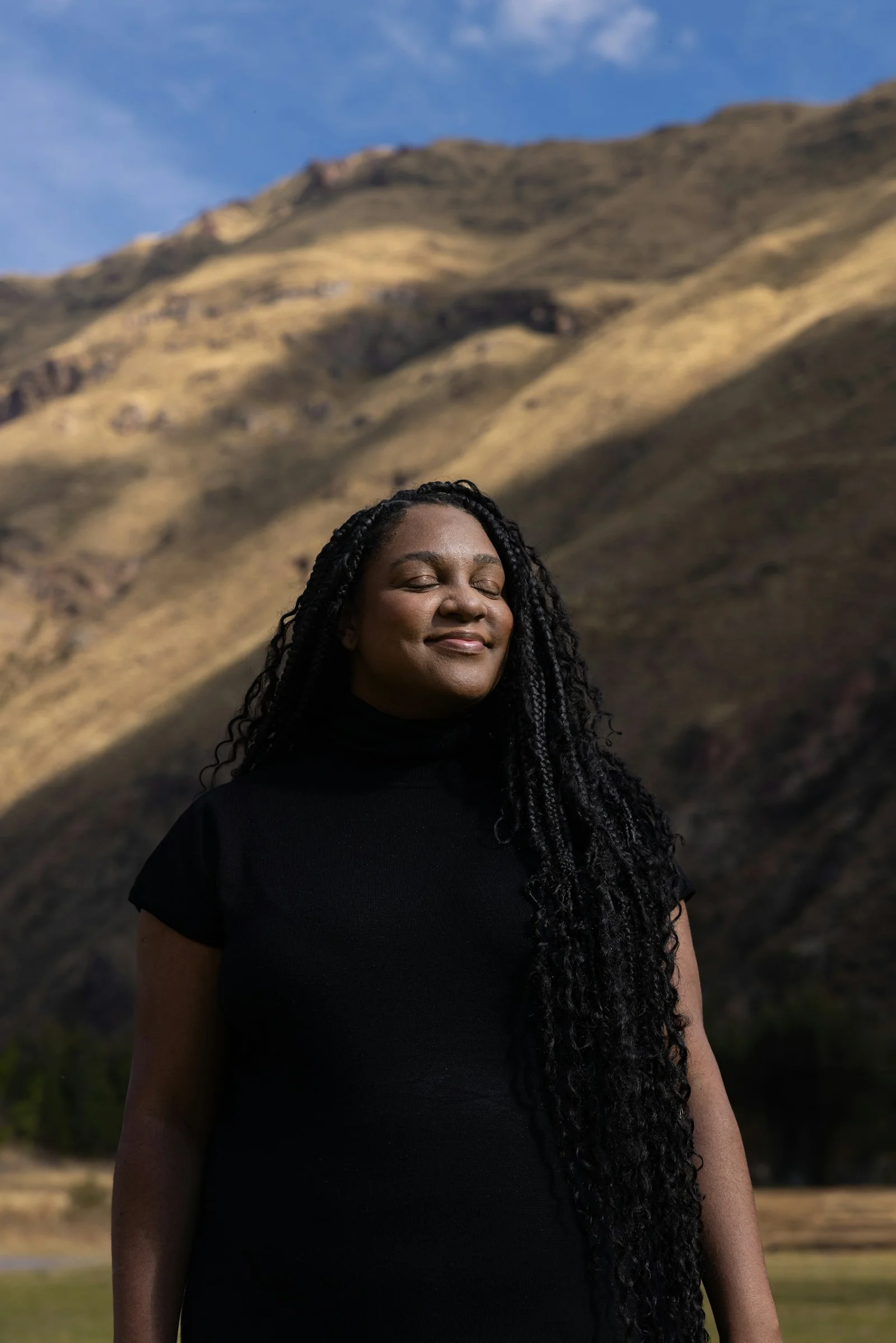 Woman smiles with eyes closed near a mountain