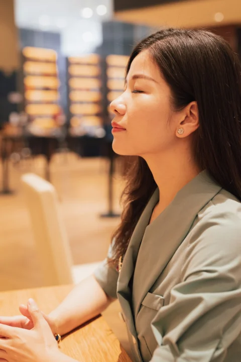 一位闭着双眼、身穿浅绿色西装外套的女士坐在木桌旁