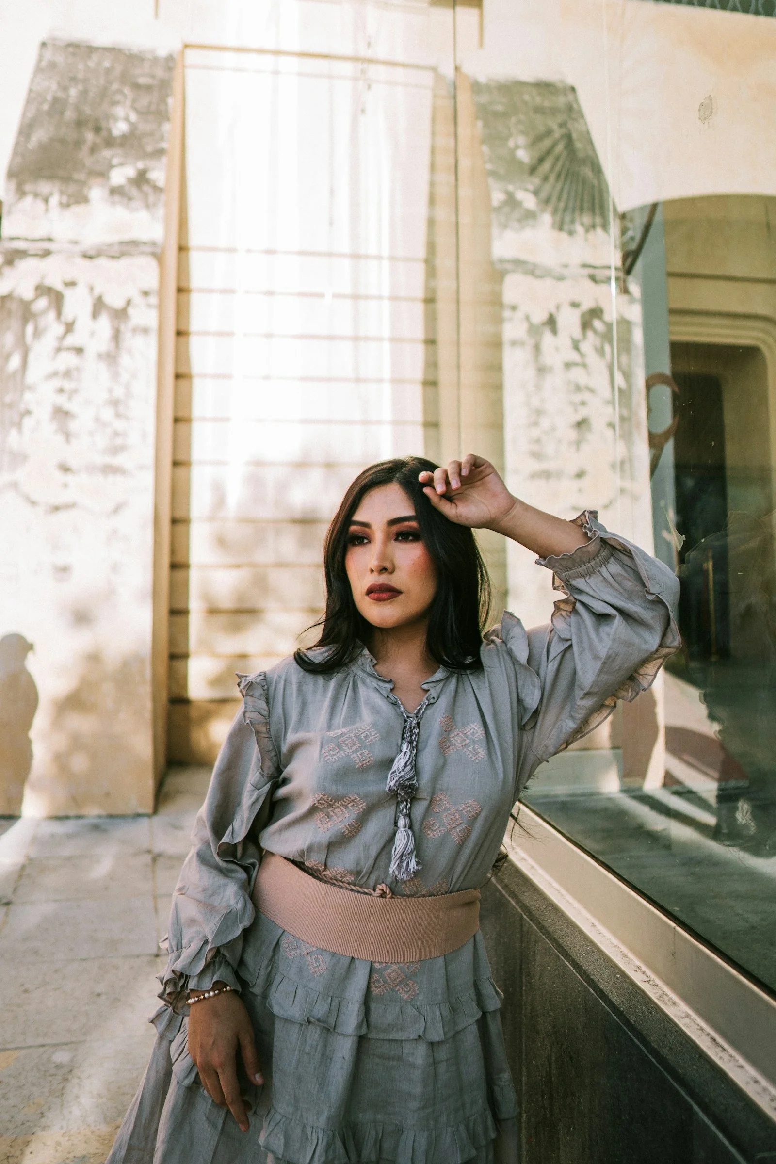 A woman poses gracefully near a weathered building