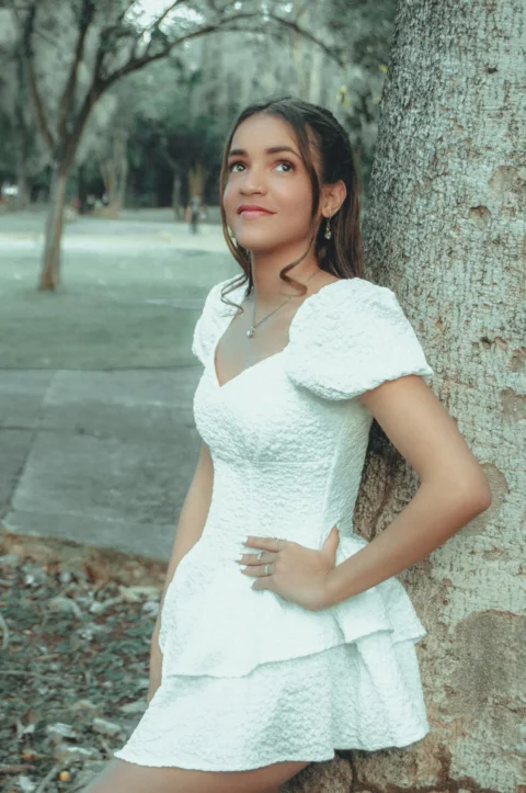 a woman in a white dress leaning against a tree