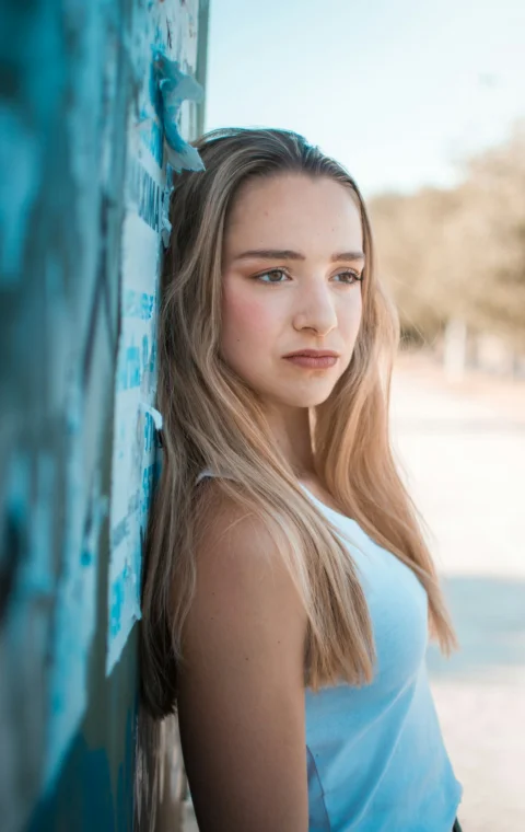 Young woman leans against a textured wall outdoors