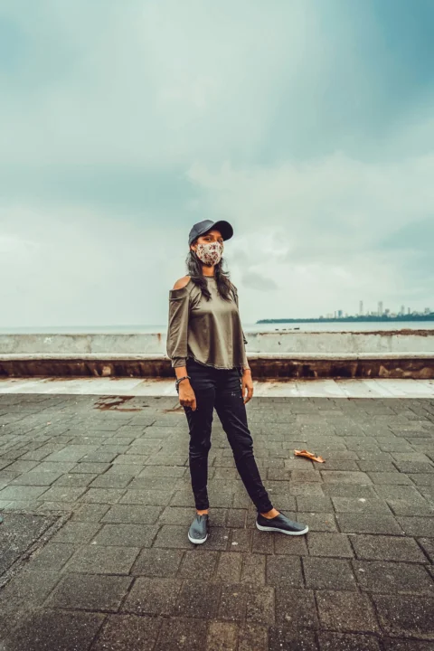 woman in gray coat and black pants standing on gray concrete pavement during daytime