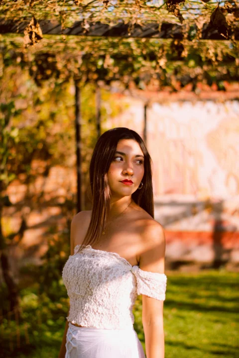 Young woman in white dress standing under foliage outdoors