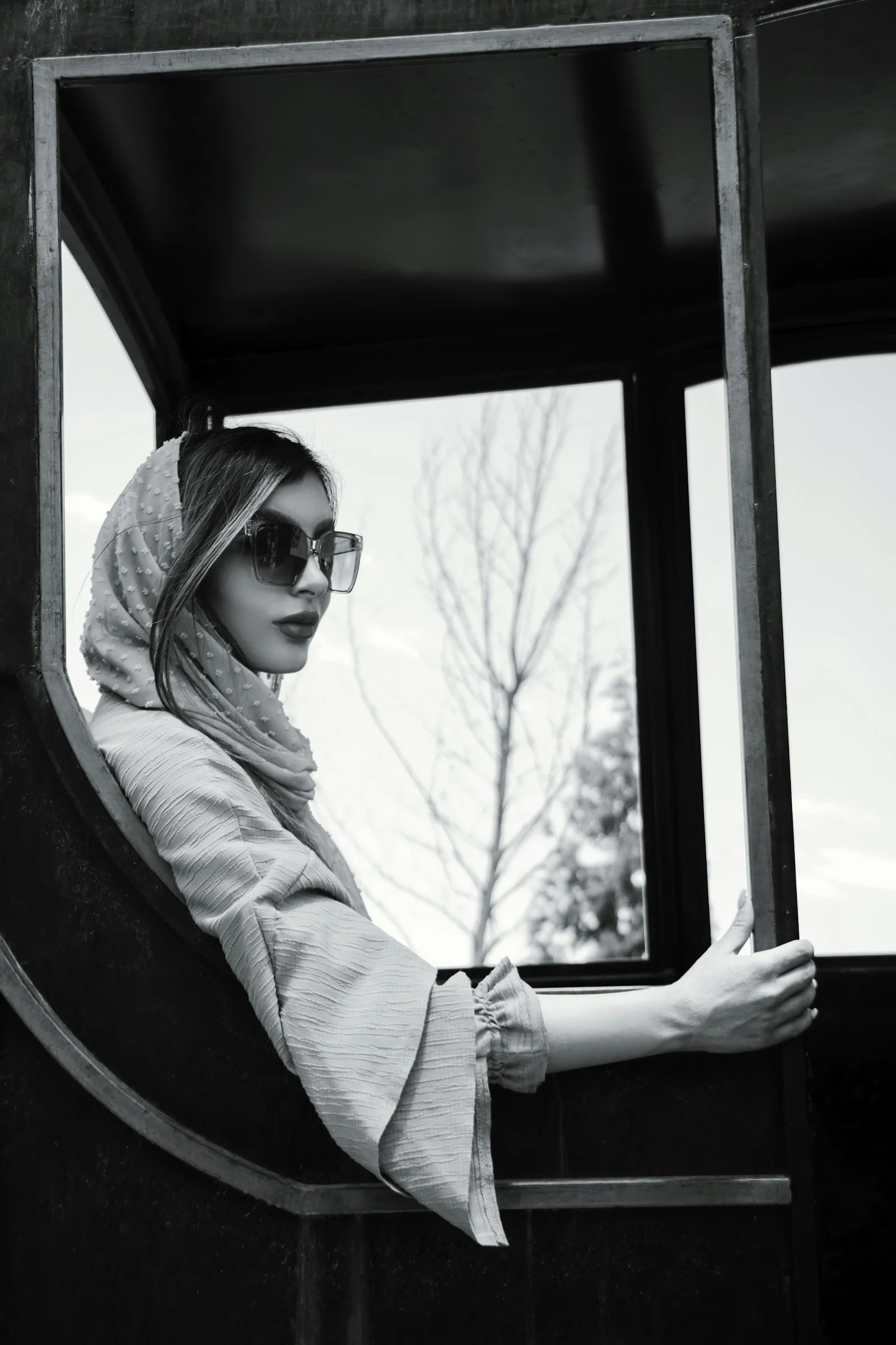 a woman wearing a scarf and sunglasses looking out a window