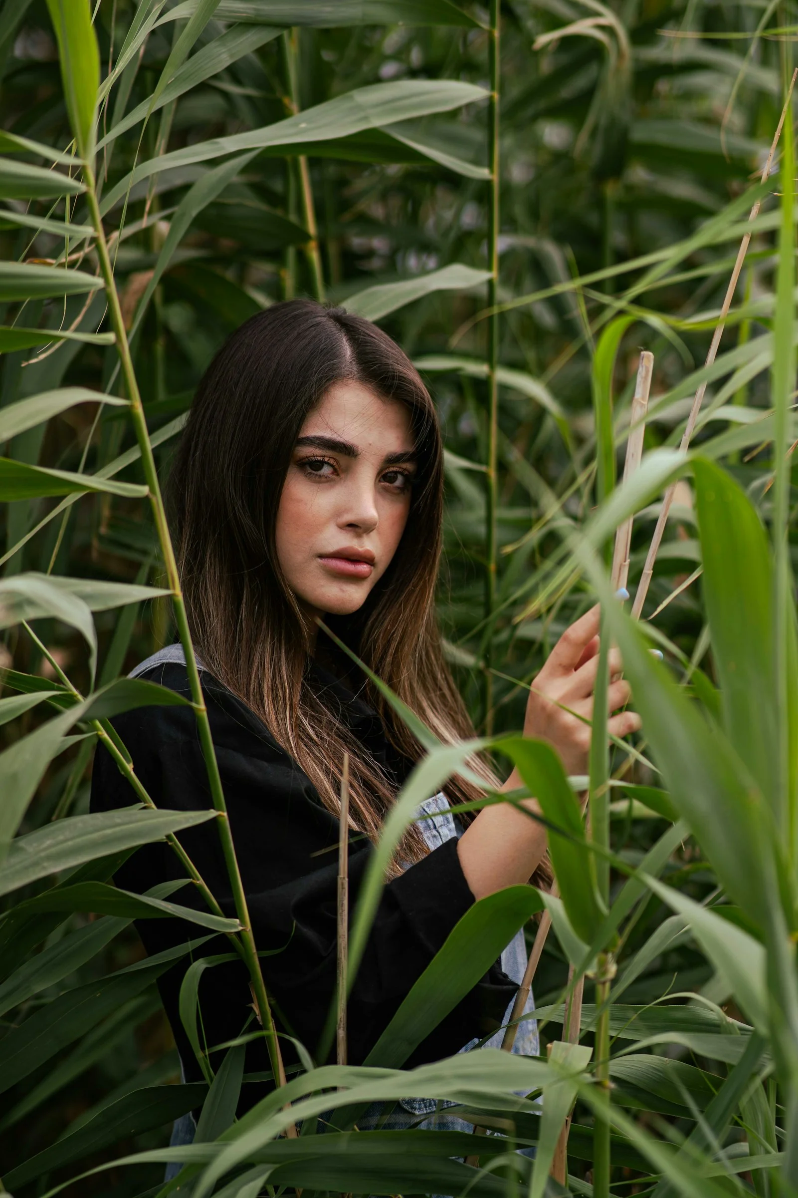 A young woman peeks through tall green reeds