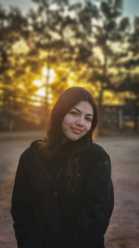 A woman standing in front of a tree at sunset