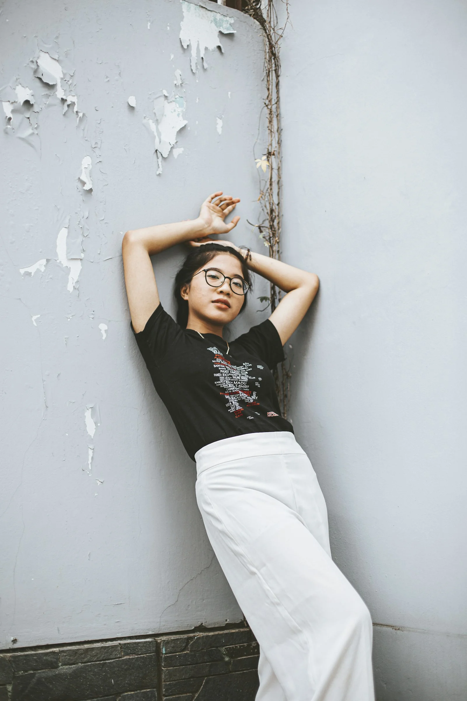 一名女子靠在牆上，雙手放在頭上