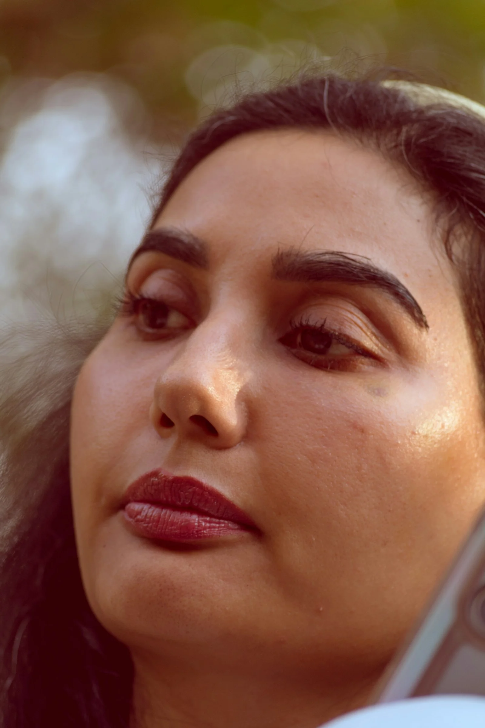 A woman with dark hair and red lipstick looking away in soft light