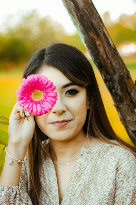 a woman holding a pink flower in front of her face