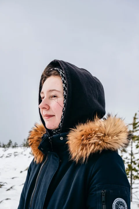 a woman standing in the snow with a hood on