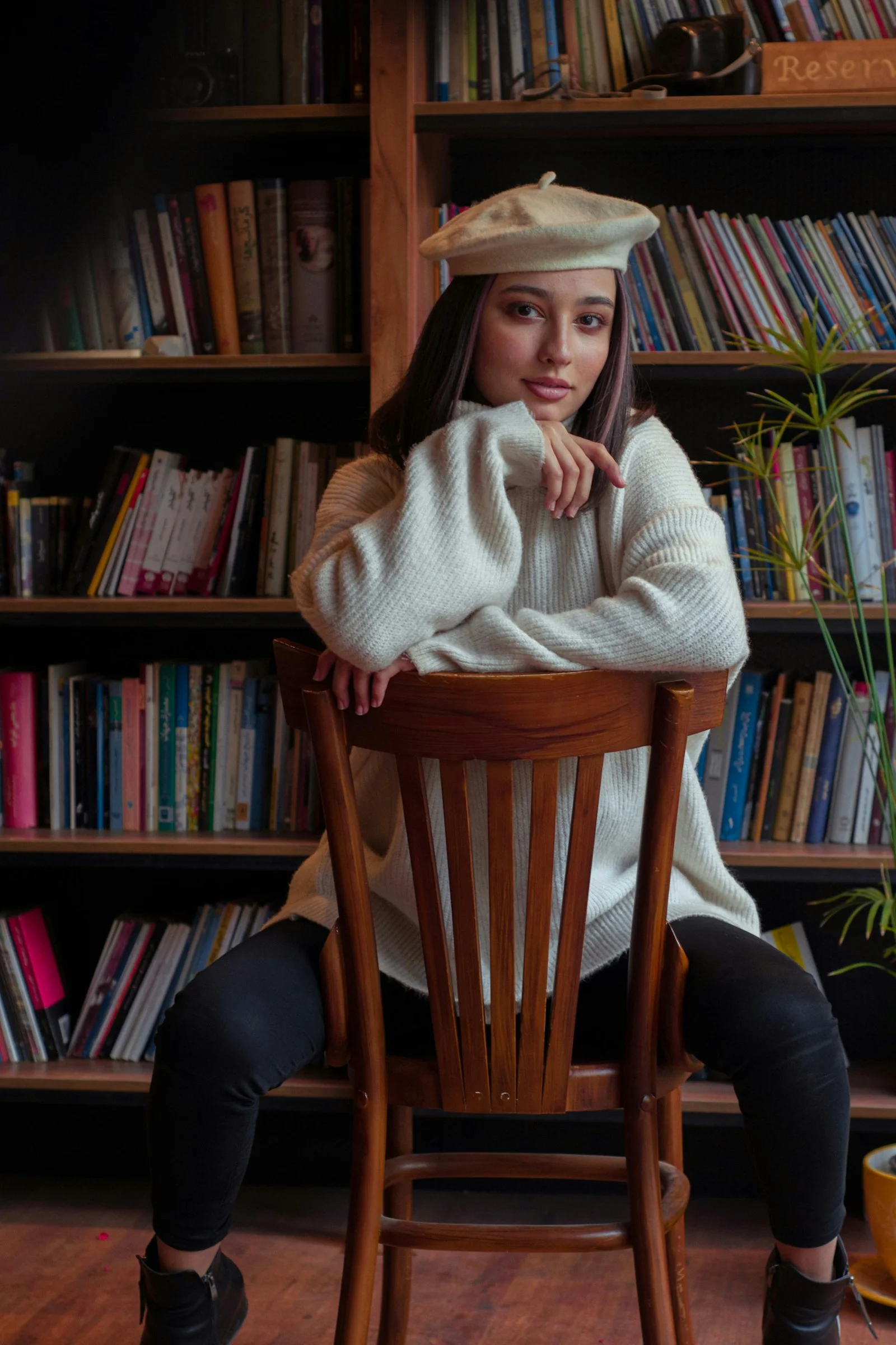 Young woman wearing a beret and sweater sits on chair