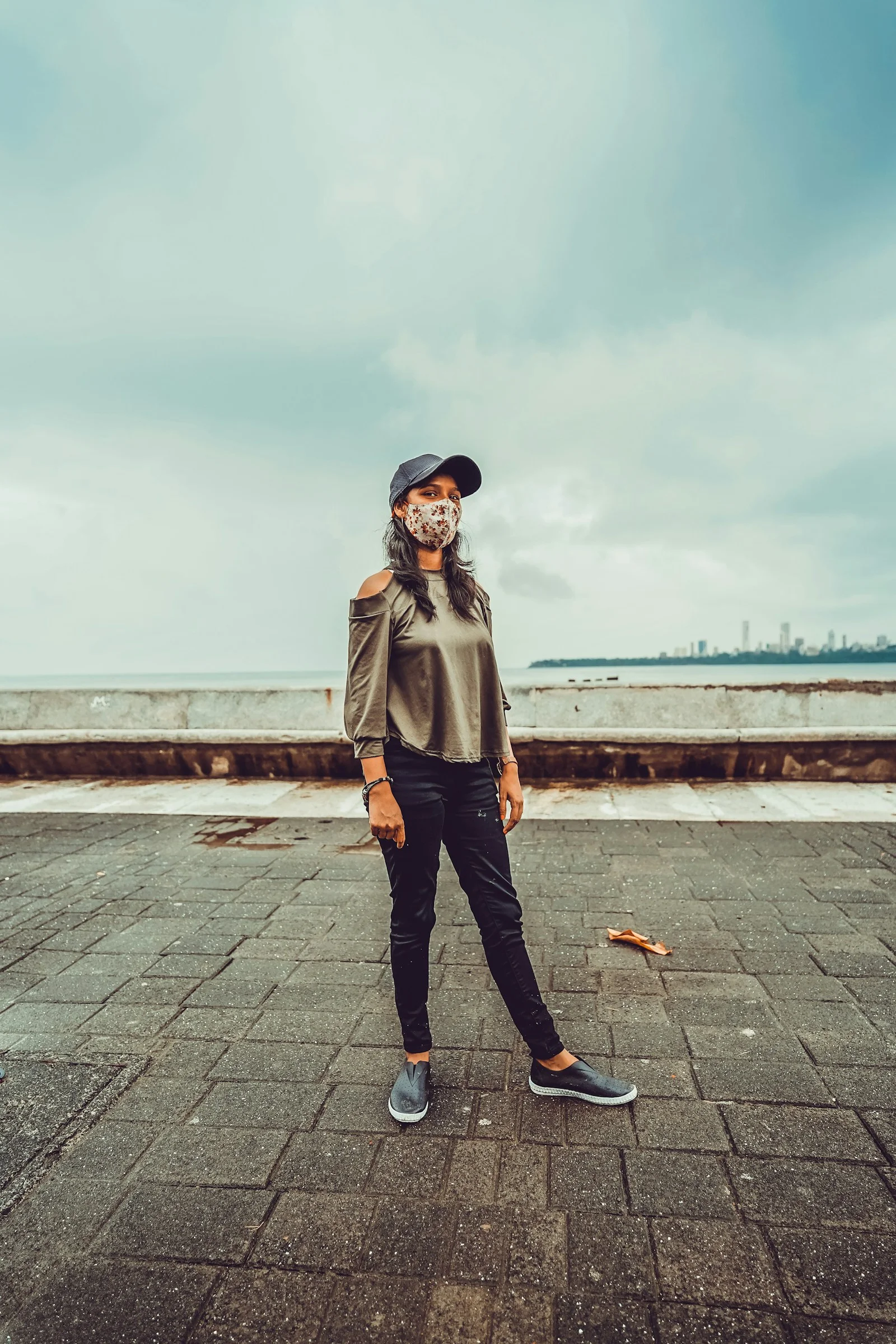 白天身穿灰色大衣和黑色長褲站在灰色混凝土鋪面上的女子
