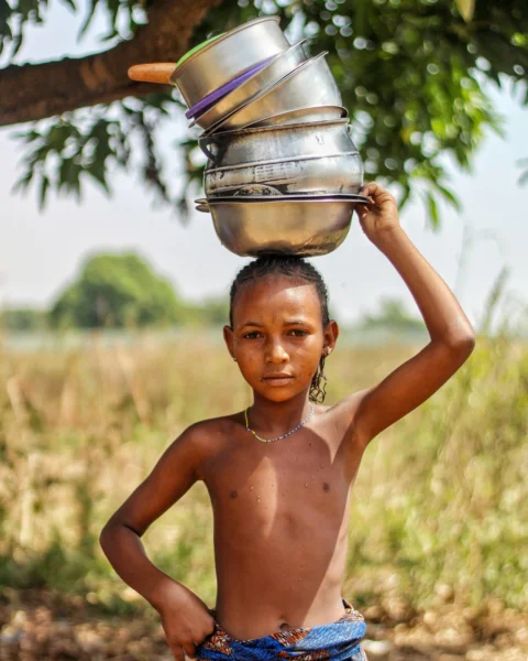 a young girl carrying a pot on her head
