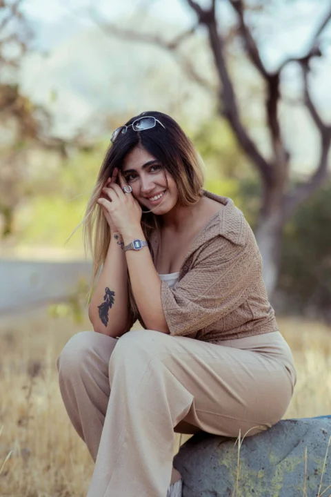 A smiling woman sits outdoors on a rock