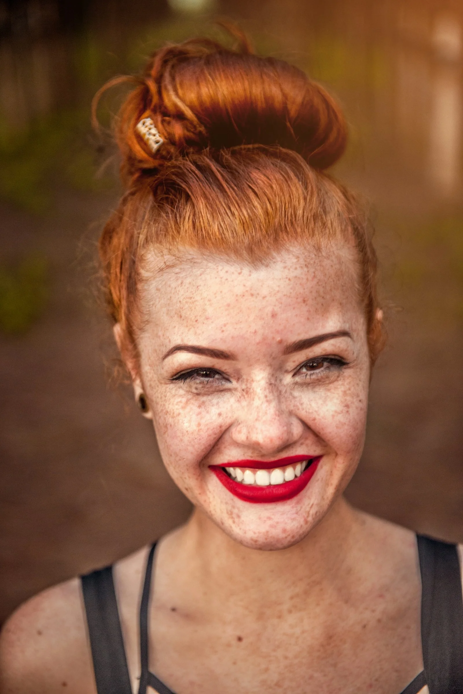 A smiling woman with red hair in a bun and visible freckles