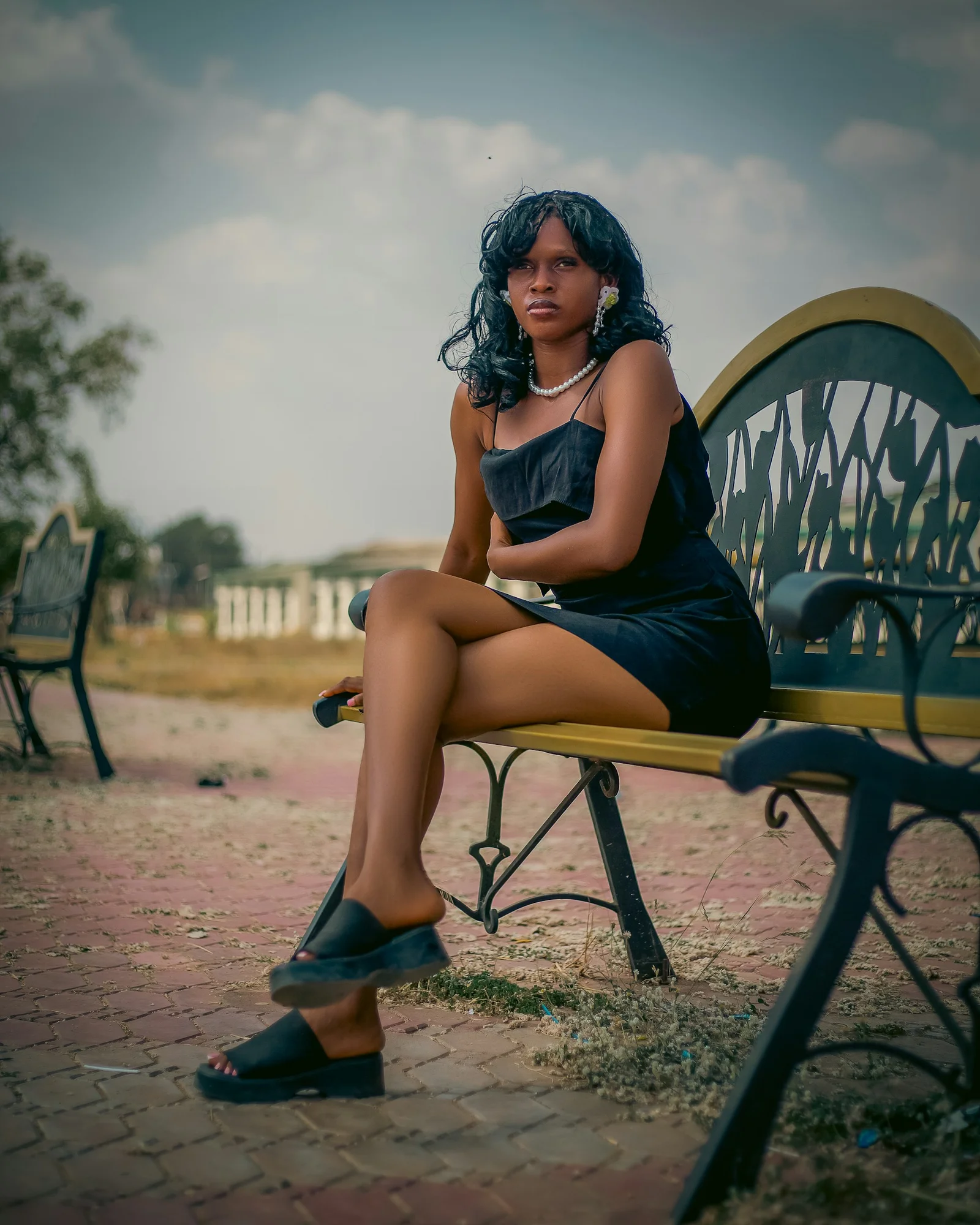Young woman in black dress sitting on park bench