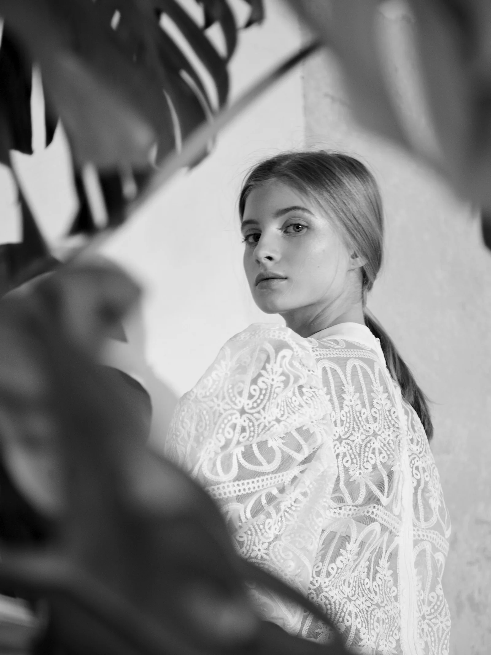 Young woman in white lace top peeking through leaves