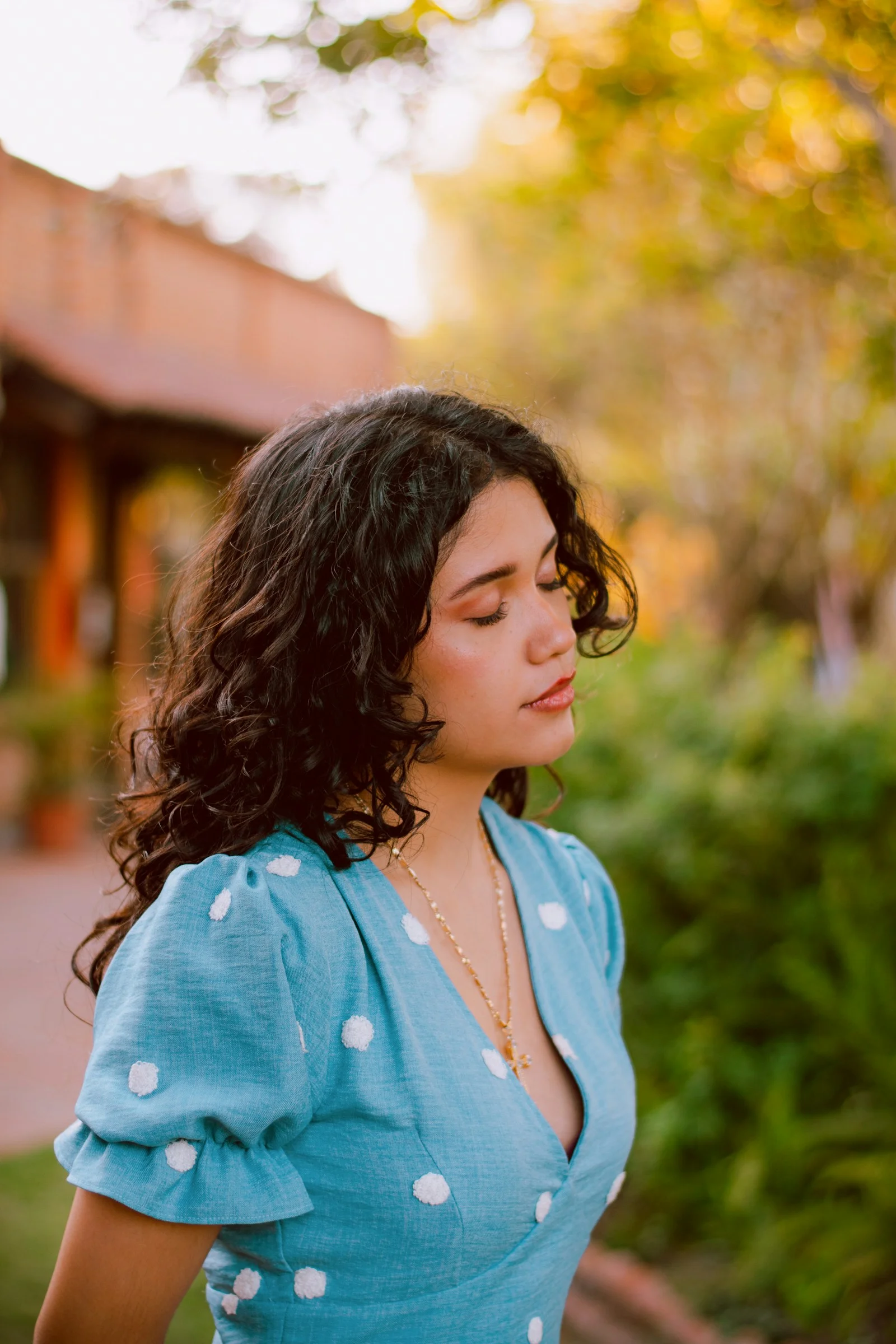 Curly-haired woman in blue polka-dot dress with eyes closed