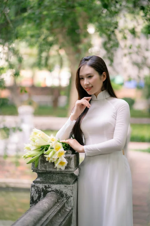 身穿白色连衣裙的年轻女子手持鲜花摆姿势