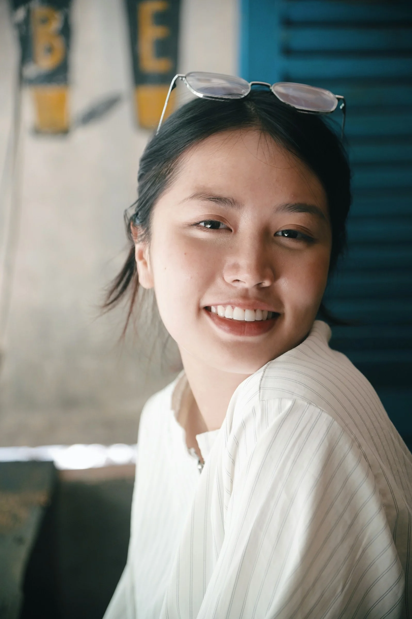 一位面带微笑的女子，眼镜架在头顶，身穿白色条纹衬衫