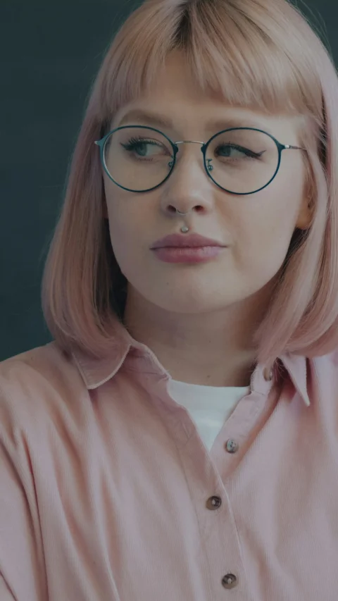 A person with pink hair and glasses wearing a pink collared shirt