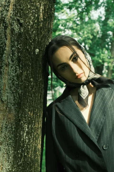 a woman standing next to a tree wearing a suit