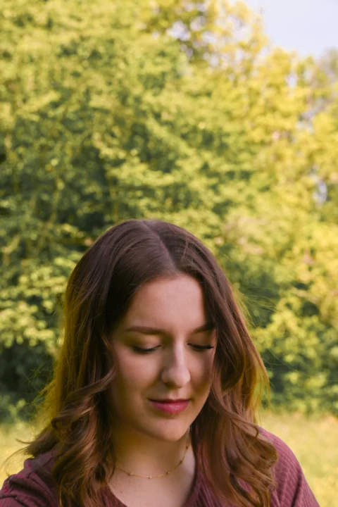 A young woman with brown hair looking down outdoors