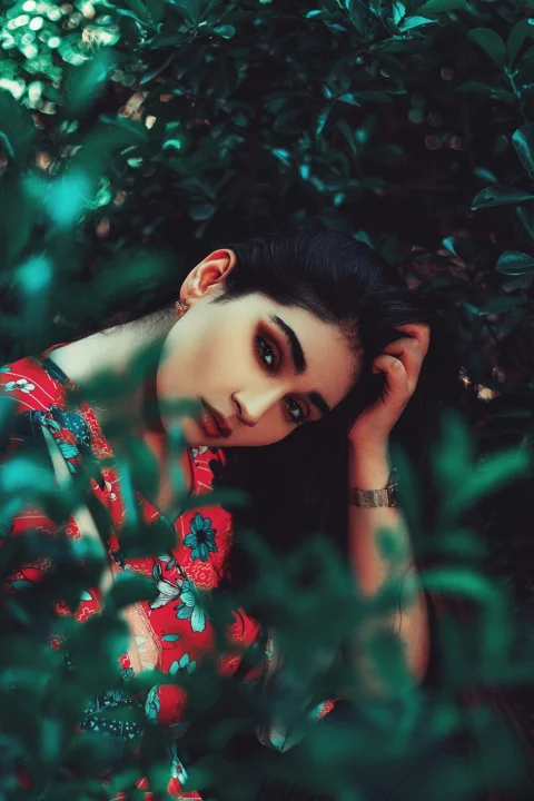 A woman in a red floral top framed by dark green foliage