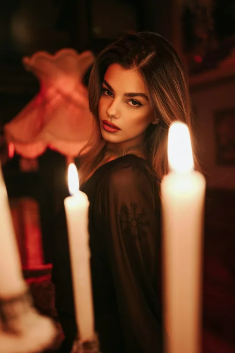 A woman in a black top with a tattoo on her arm by candlelight
