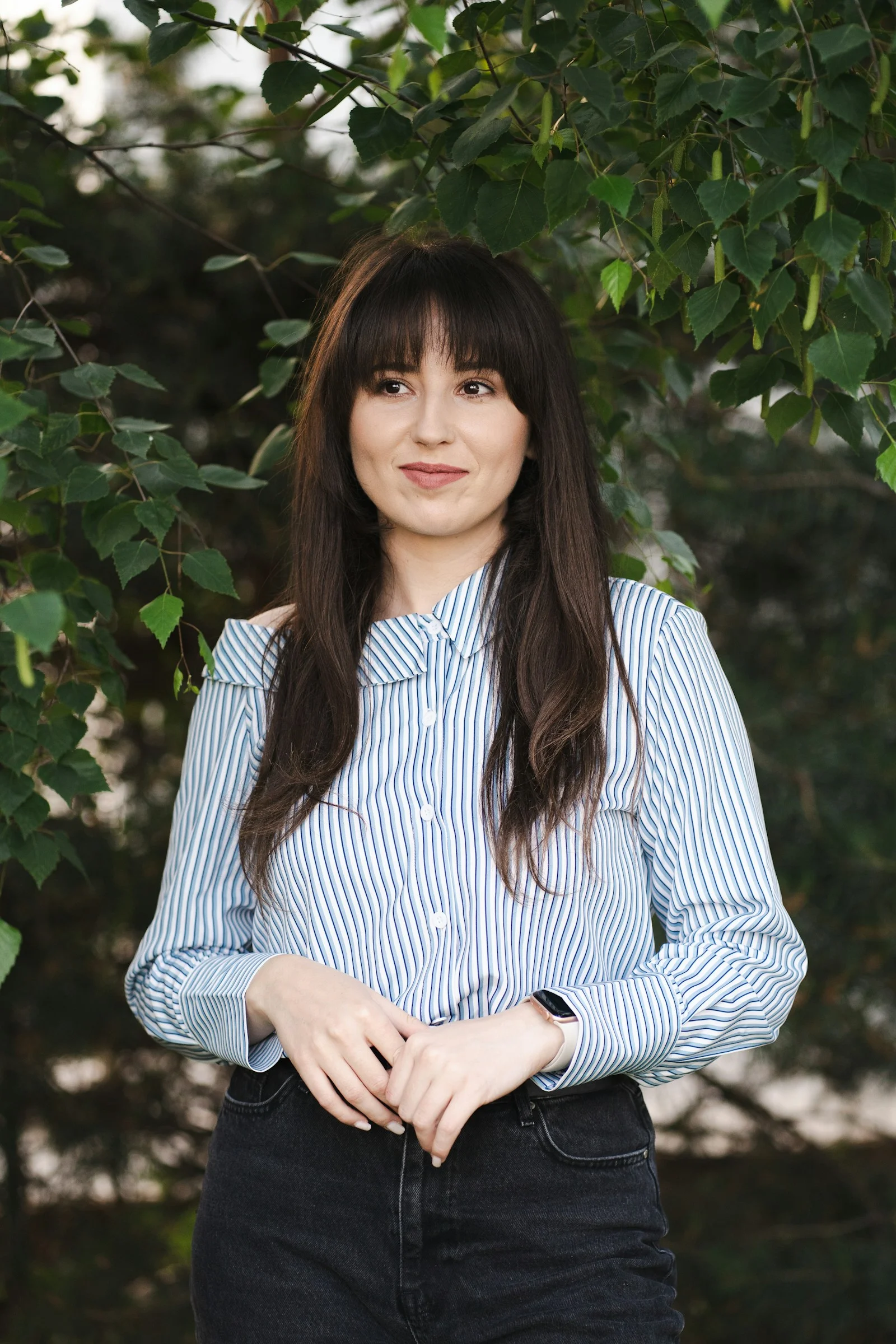 Woman smiles while posing near foliage