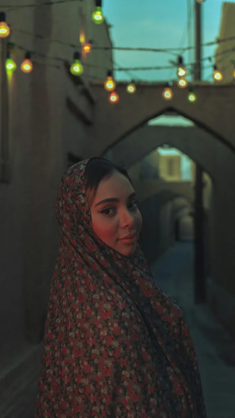 A woman wearing a headscarf in a dimly lit alley