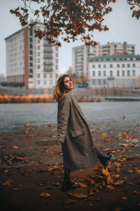 a woman standing in front of a tree with leaves on the ground