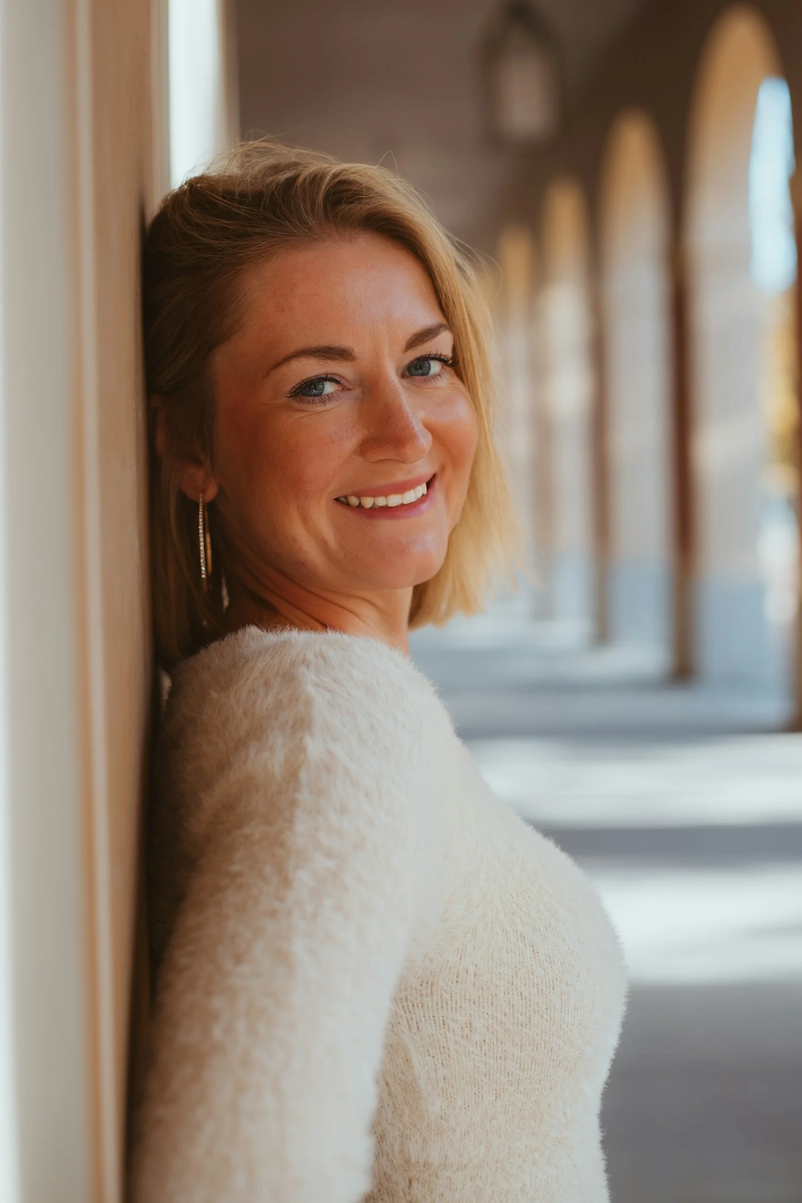 A woman leaning against a wall smiling at the camera