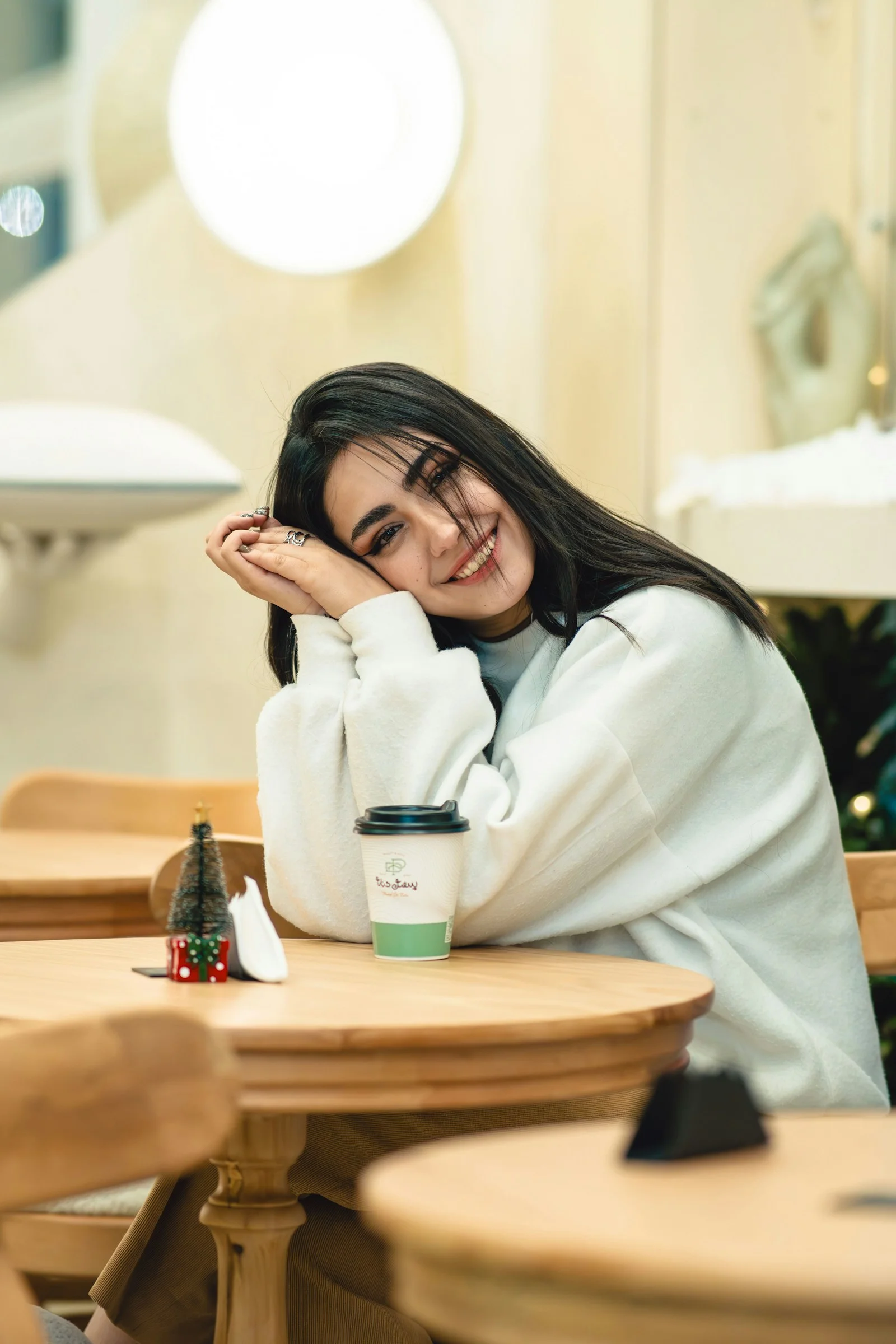 A smiling woman sits at a cafe table with coffee
