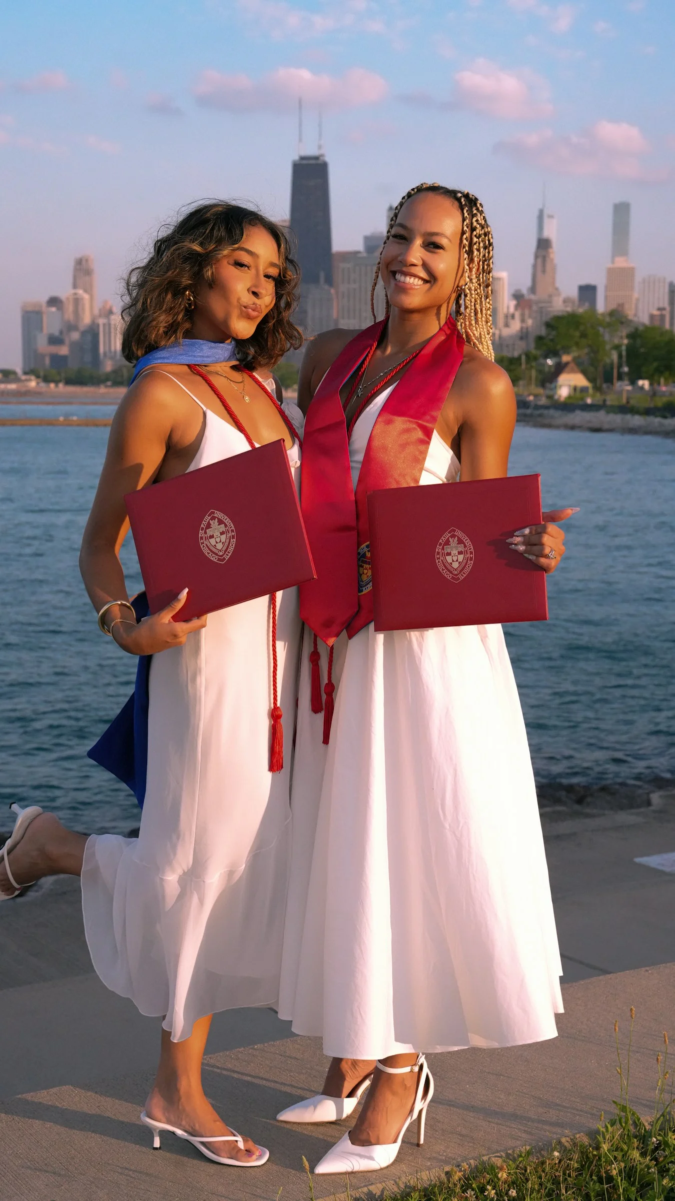 Two beautiful women standing next to each other in front of a body of water