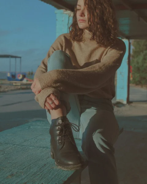 woman in brown sweater and black pants sitting on concrete floor during daytime