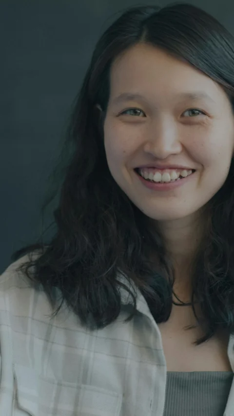 A smiling woman with long dark wavy hair wearing a plaid shirt