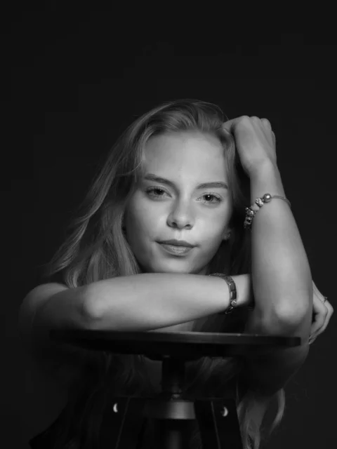 Young woman with long blonde hair resting arms on stool